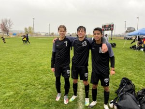 3 boys pose on the soccer field