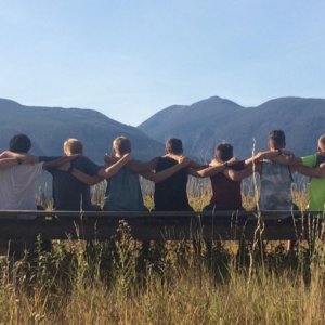 A picture of the Cross Country team sitting on a fence with the Bitterroot Mountains in the background