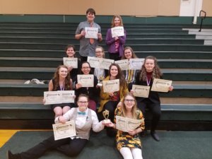 A photo of the Speech, Debate, Drama team seated in bleachers holding their awards following the Winter 2018 Stevensville Competition