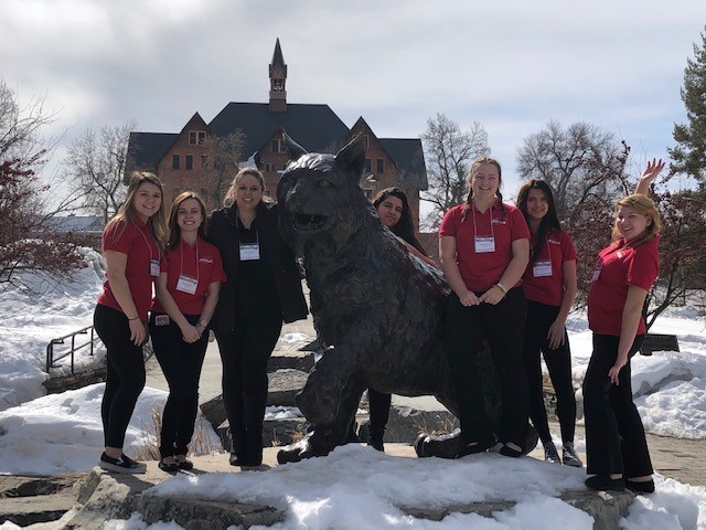 A photo of six of our FCCLA members at Montana State University outside in red shhirts standing next to a statue of a bobcat