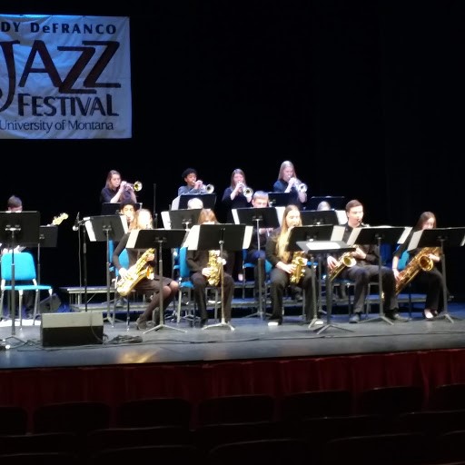 The jazz band performing on a state with a black background, Saxophones can be seen in the front row and trumpets in the row.