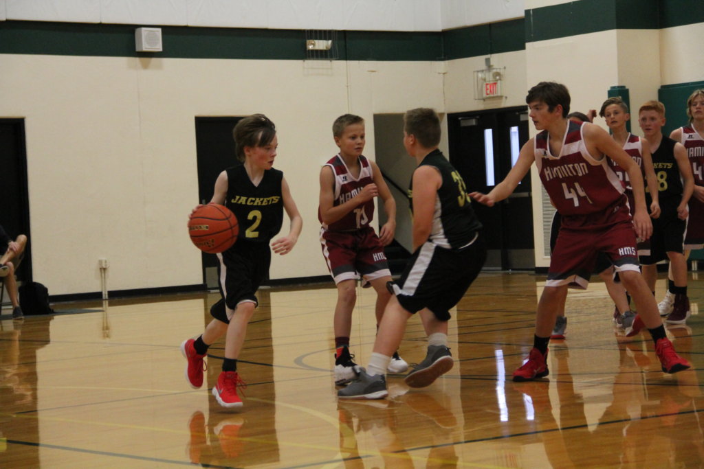 A stevensville middle school payer dribbles the ball while a teammate sets a pick to disrupt two defenders from Hamilton