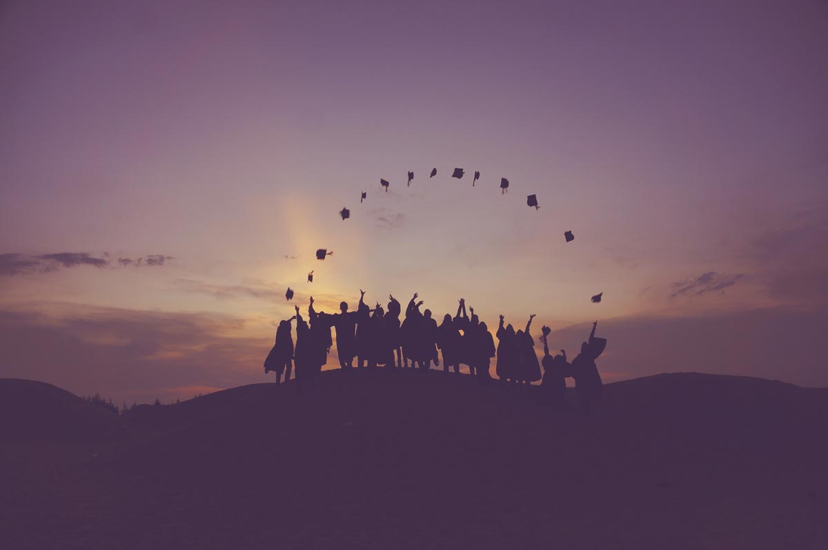 Photo of High School Graduated throwing their caps in front of sunset